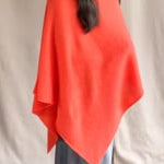 video of a woman wearing a cashmere cape in orange with matching cashmere beanie hat over grey silk skirt