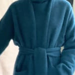 video of a woman wearing a long cashmere coat in teal blue over teal blue cashmere turtleneck sweater and bronze silk trousers