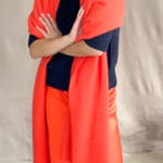 a video of a woman wearing a large cashmere wrap in orange over a cashmere aran sweater tee in navy blue with orange silk skirt
