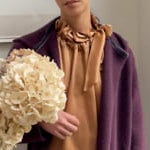 video of a woman wearing a bronze pussy bow silk blouse with matching silk trousers and cashmere coat cardigan in dark purple