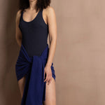A woman wears a navy blue swimsuit with a bright blue cashmere shawl wrapped around her waist as a pareo skirt
