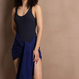 A woman wears a navy blue swimsuit with a bright blue cashmere shawl wrapped around her waist as a pareo skirt