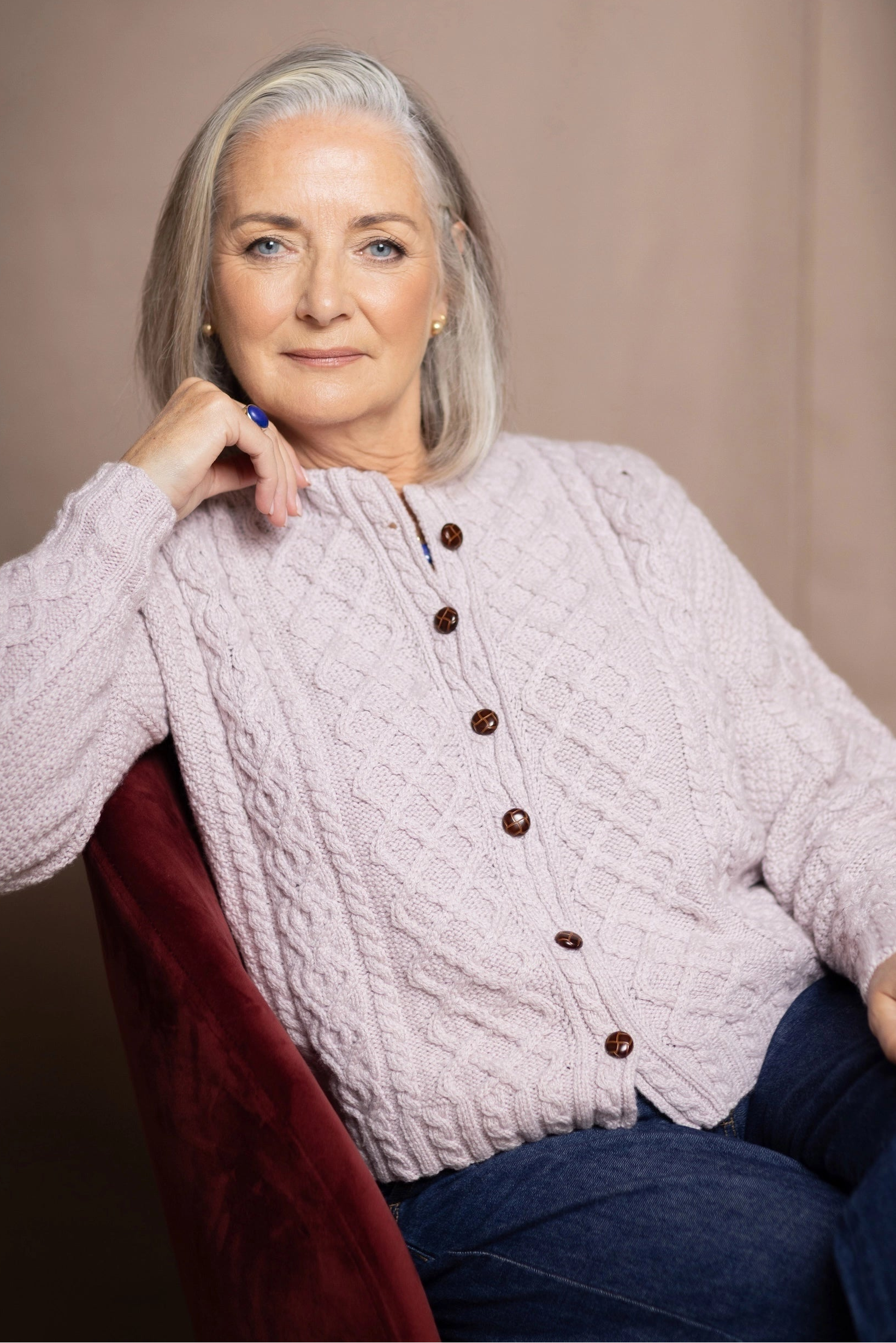 A woman wearing a cashmere aran cable-knit button-up cardigan sweater in light pink over jeans