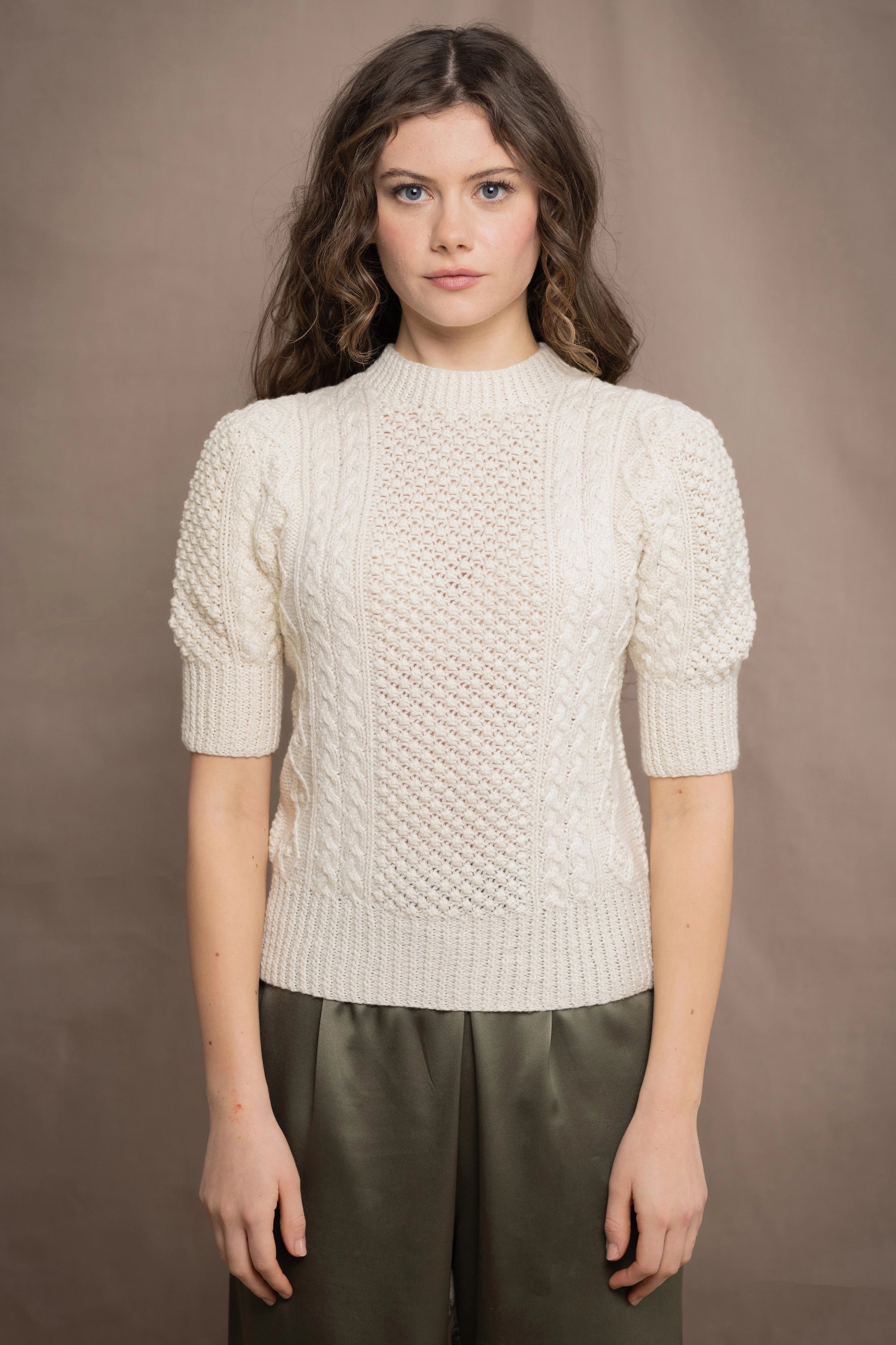 Woman wearing a cream knitted cashmere aran sweater from Ireland and green silk pants