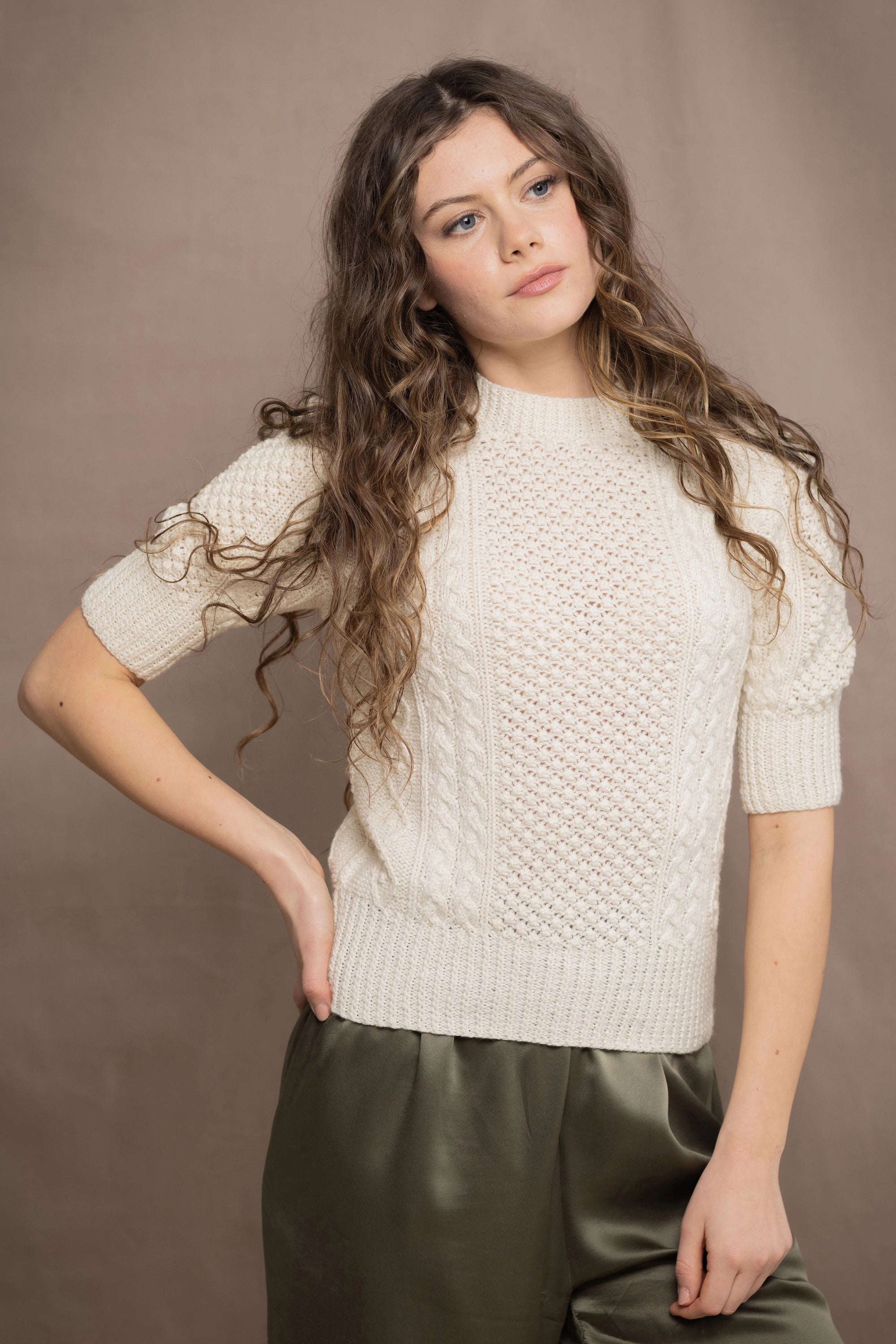 Woman wearing a cream knitted cashmere aran sweater from Ireland and green silk pants
