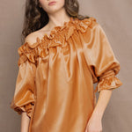 Woman wearing a bronze silk top with ruffle details