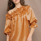 Woman wearing a bronze silk top with ruffle details