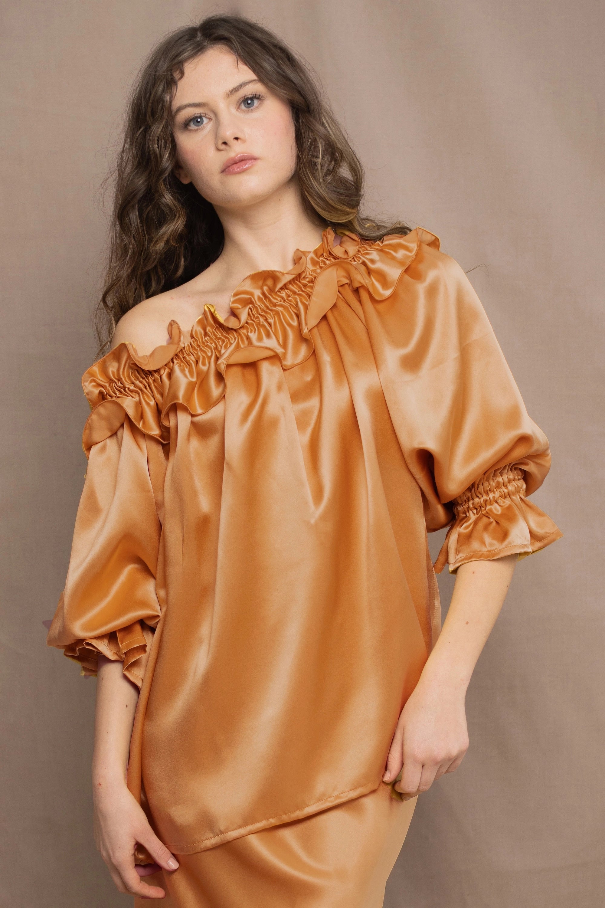 Woman wearing a bronze silk top with ruffle details