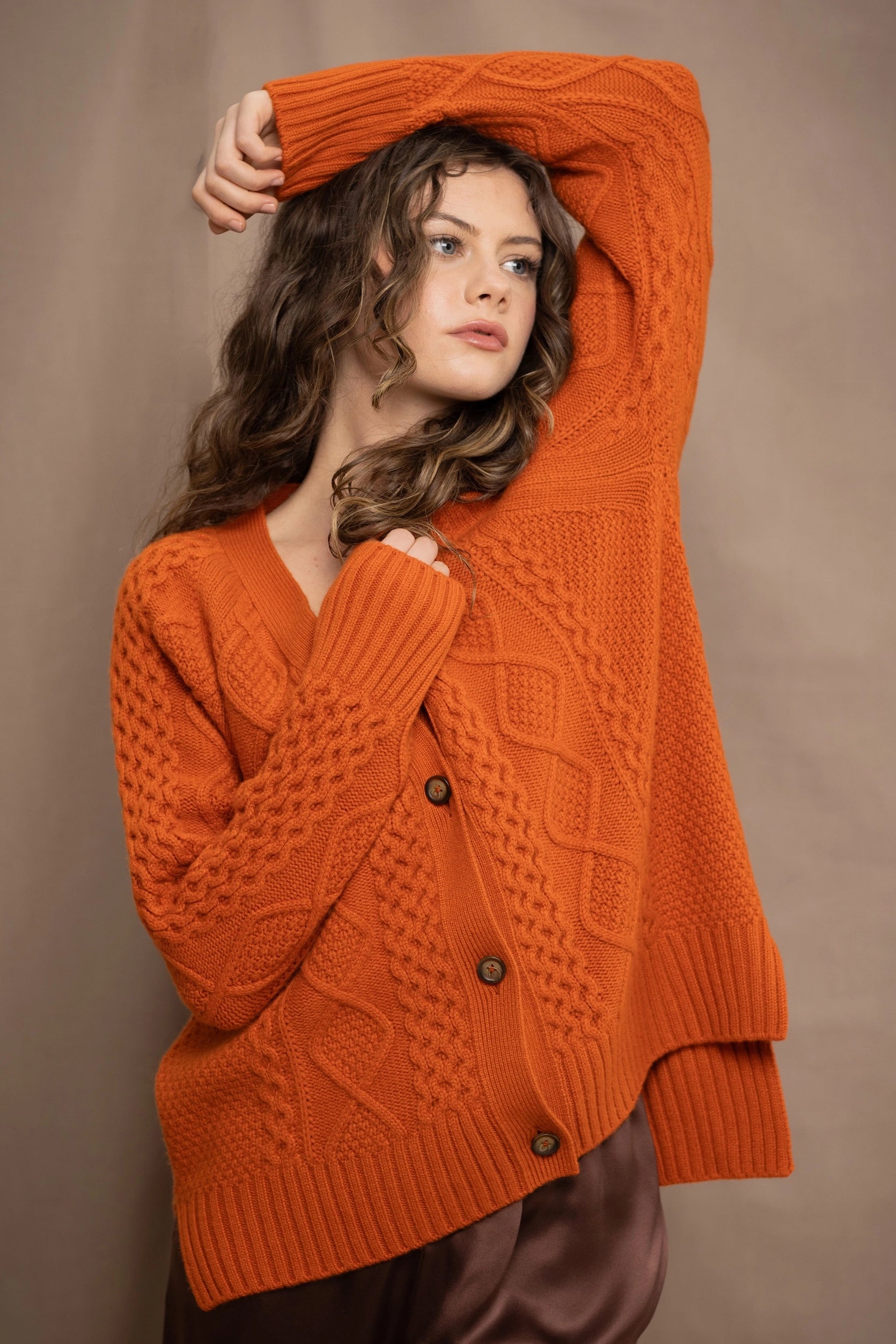 A woman wearing a chunky Irish cable-knit orange cashmere aran cardigan sweater