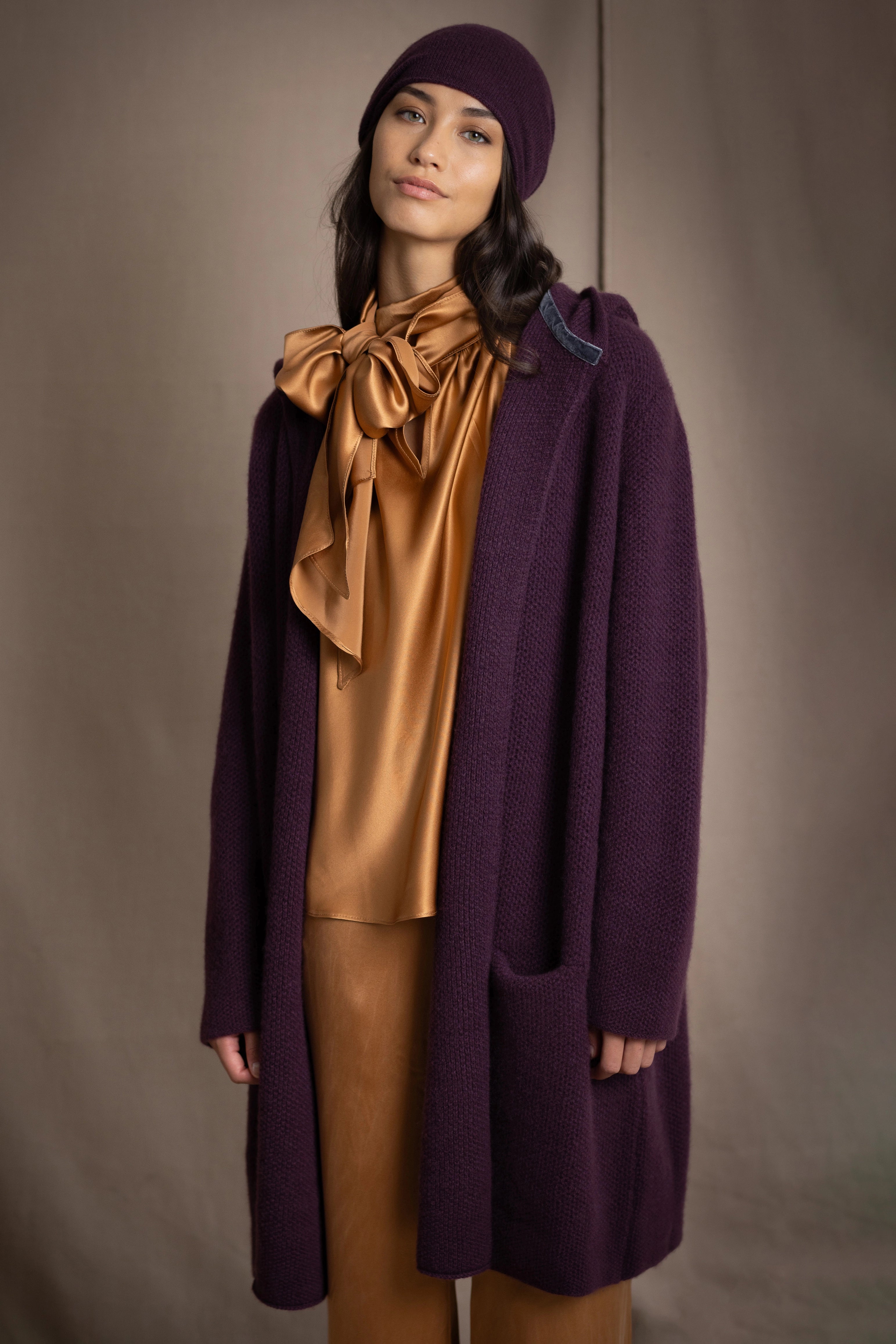 Woman wearing a purple cashmere coat and hat with a gold silk blouse
