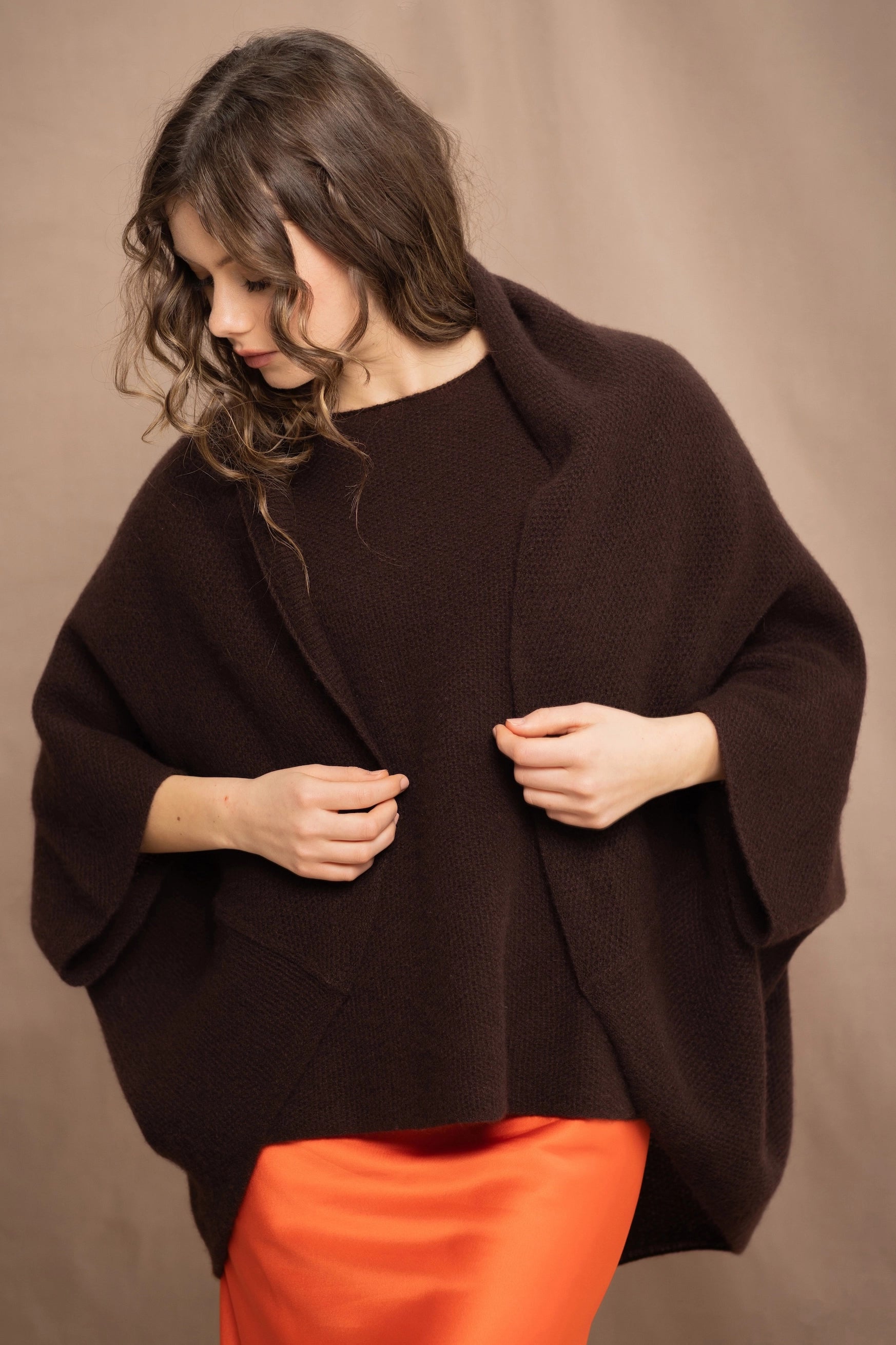 A woman wearing a dark brown open-front cashmere cardigan over a matching sweater tee and orange silk skirt