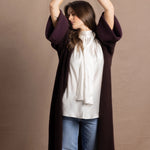A woman wears a 100% silk pussybow sleeveless blouse in white with a chocolate brown and purple cashmere coat on top