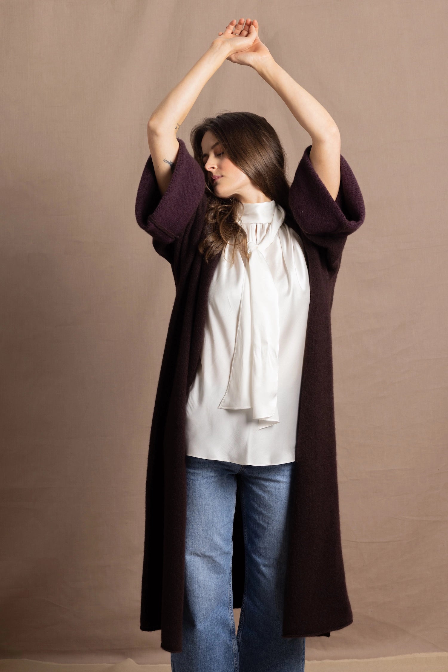 A woman wears a 100% silk pussybow sleeveless blouse in white with a chocolate brown and purple cashmere coat on top
