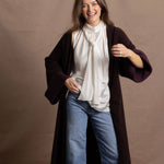 A woman wears a 100% silk pussybow sleeveless blouse in white with a chocolate brown and purple cashmere coat on top