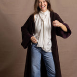 A woman wears a 100% silk pussybow sleeveless blouse in white with a chocolate brown and purple cashmere coat on top