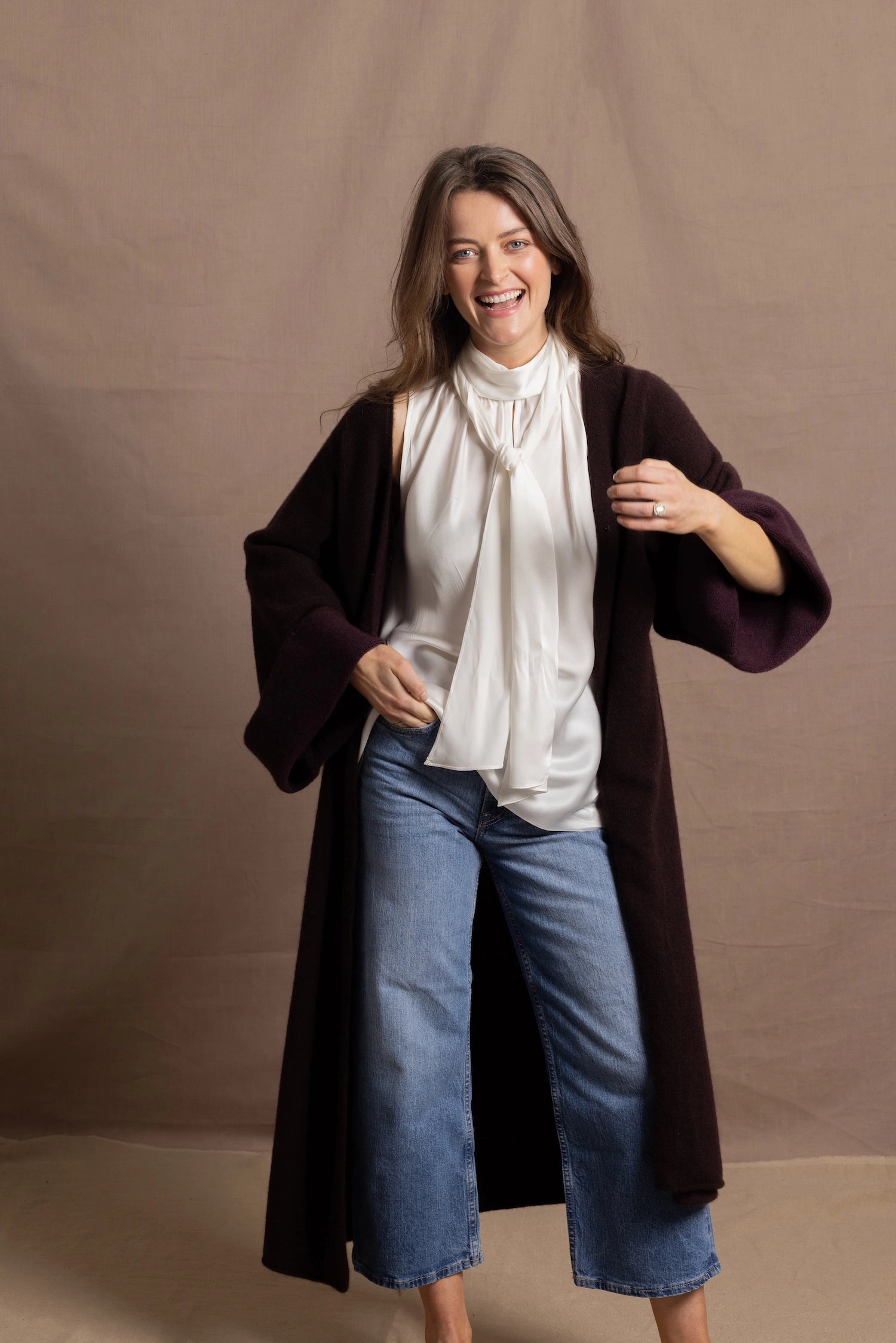 A woman wears a 100% silk pussybow sleeveless blouse in white with a chocolate brown and purple cashmere coat on top
