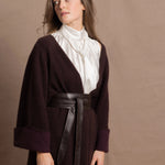 A woman wears a 100% silk pussybow sleeveless blouse in white with a chocolate brown and purple cashmere coat on top and cinched with leather obi belt