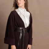 A woman wears a 100% silk pussybow sleeveless blouse in white with a chocolate brown and purple cashmere coat on top and cinched with leather obi belt