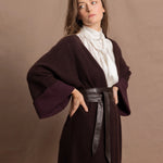A woman wears a 100% silk pussybow sleeveless blouse in white with a chocolate brown and purple cashmere coat on top and cinched with leather obi belt