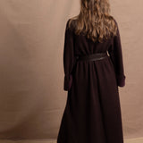 A woman wears a 100% silk pussybow sleeveless blouse in white with a chocolate brown and purple cashmere coat on top and cinched with leather obi belt