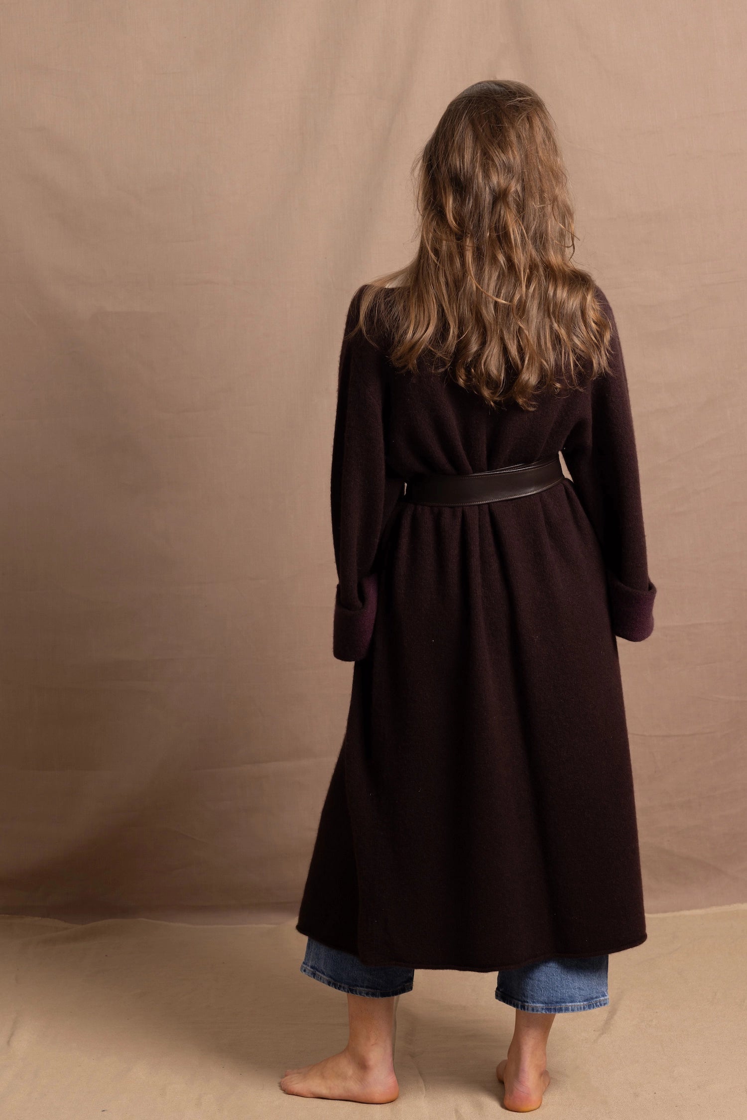 A woman wears a 100% silk pussybow sleeveless blouse in white with a chocolate brown and purple cashmere coat on top and cinched with leather obi belt