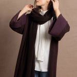 A woman wears a 100% silk pussybow sleeveless blouse in white with a chocolate brown and purple cashmere coat on top with matching wrap