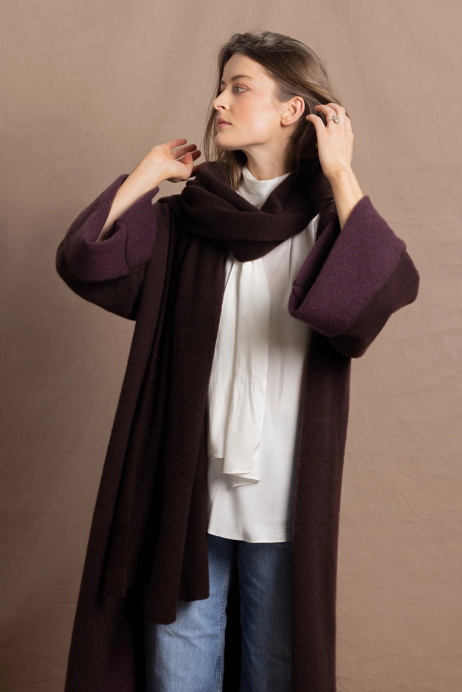 A woman wears a 100% silk pussybow sleeveless blouse in white with a chocolate brown and purple cashmere coat on top with matching wrap