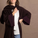 A woman wears a 100% silk pussybow sleeveless blouse in white with a chocolate brown and purple cashmere coat on top with matching wrap