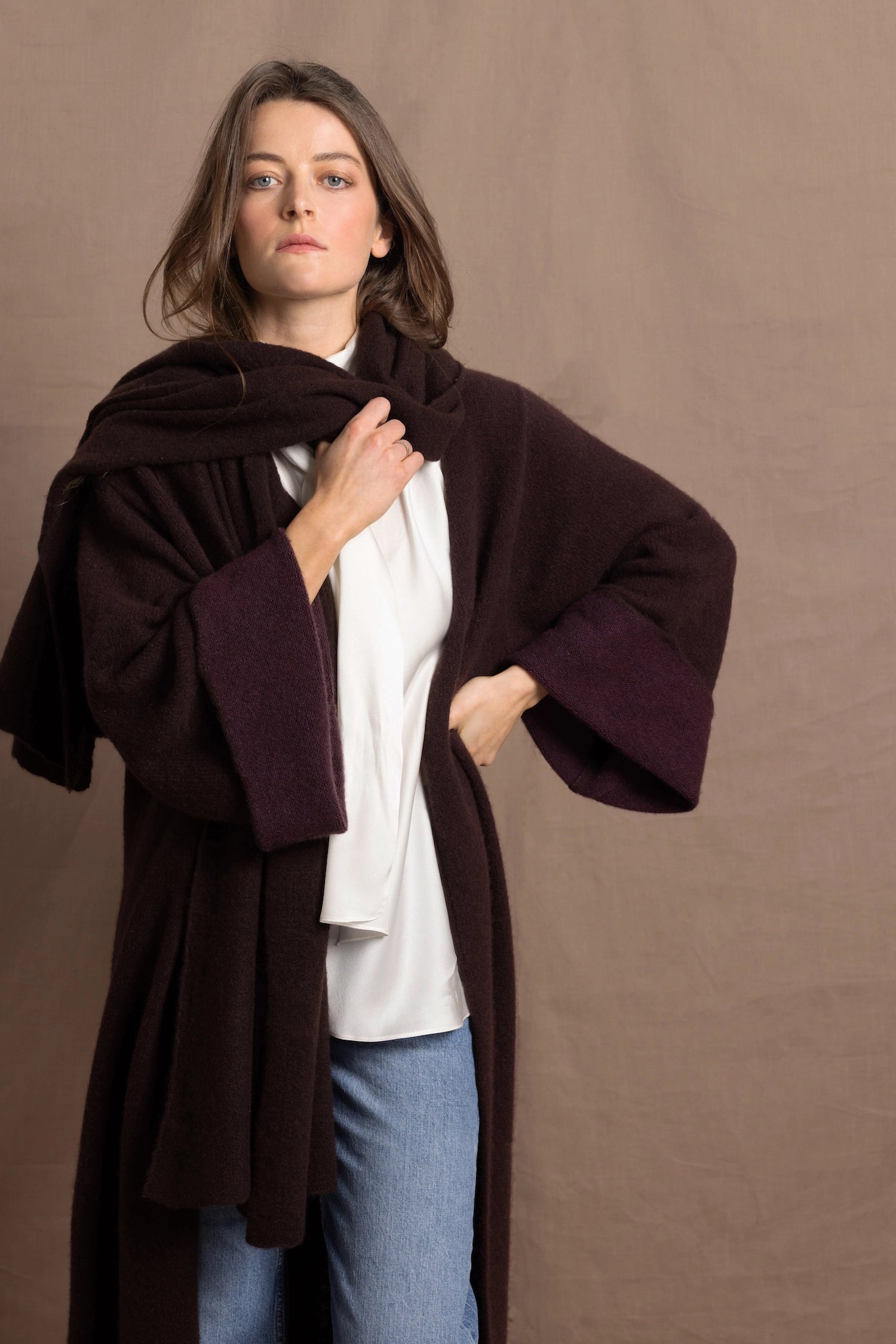 A woman wears a 100% silk pussybow sleeveless blouse in white with a chocolate brown and purple cashmere coat on top with matching wrap