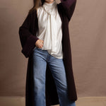 A woman wears a 100% silk pussybow sleeveless blouse in white with a chocolate brown and purple cashmere coat on top