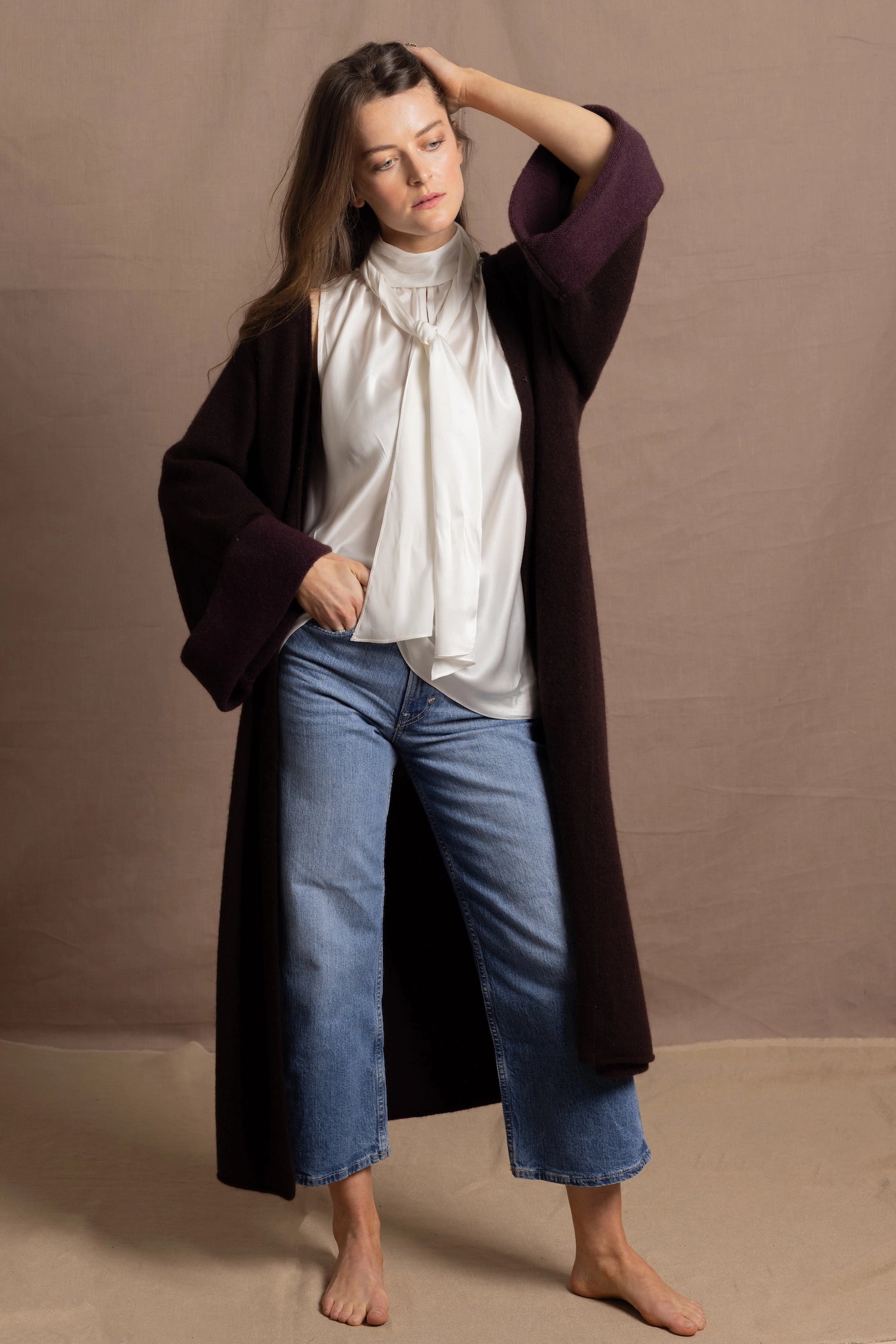 A woman wears a 100% silk pussybow sleeveless blouse in white with a chocolate brown and purple cashmere coat on top