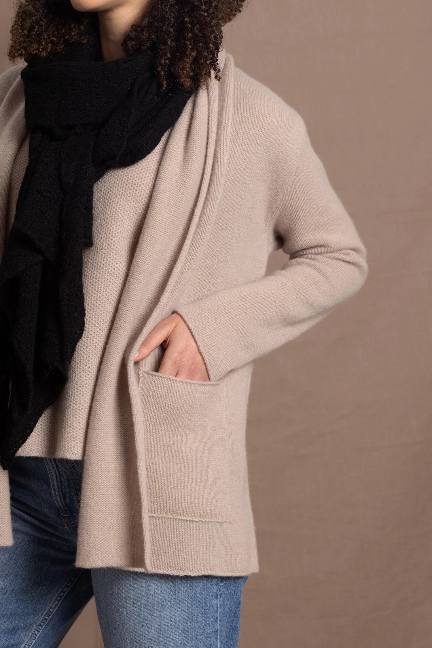 Lady wears beige coloured open cashmere cardigan over matching cashmere tee  and black scarf