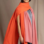 a woman wears a large cashmere wrap shawl in bright orange layered with a cashmere wrap in dusty rose pink
