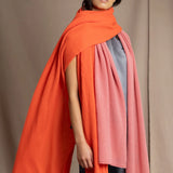 a woman wears a large cashmere wrap shawl in bright orange layered with a cashmere wrap in dusty rose pink