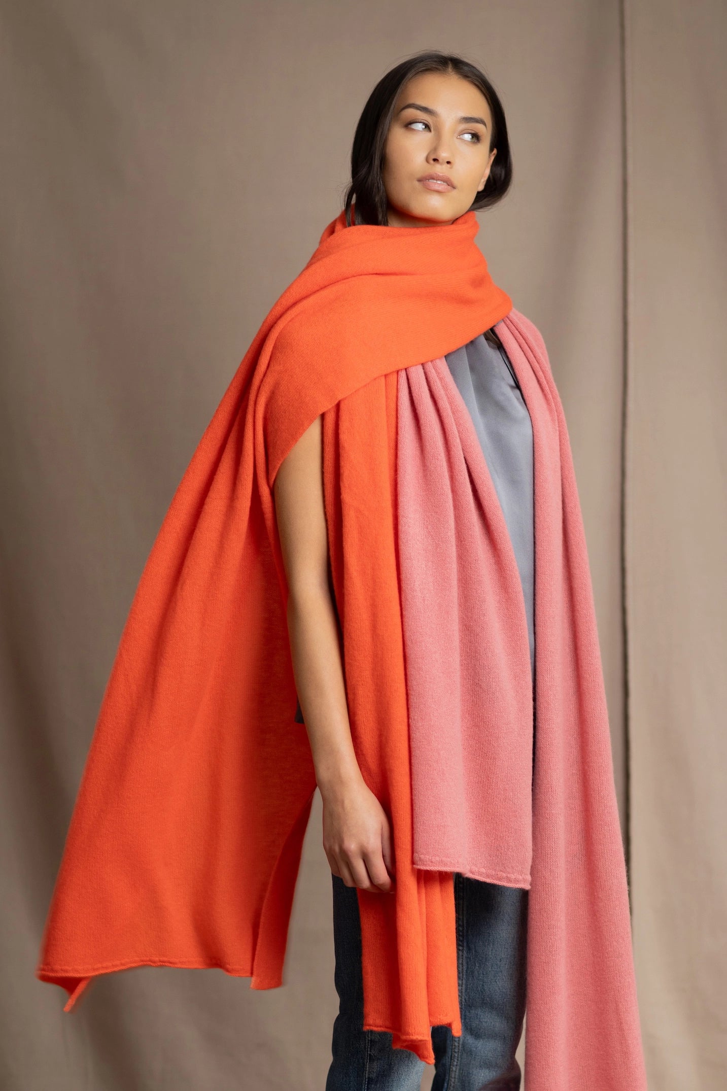 a woman wears a large cashmere wrap shawl in bright orange layered with a cashmere wrap in dusty rose pink