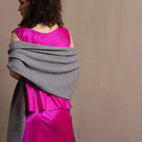 Lady wears large cashmere wrap shawl in Grey against bright pink silk clothing
