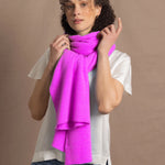a woman wears a neon pink cashmere scarf wrapped up around her neck over a white silk tee with jeans