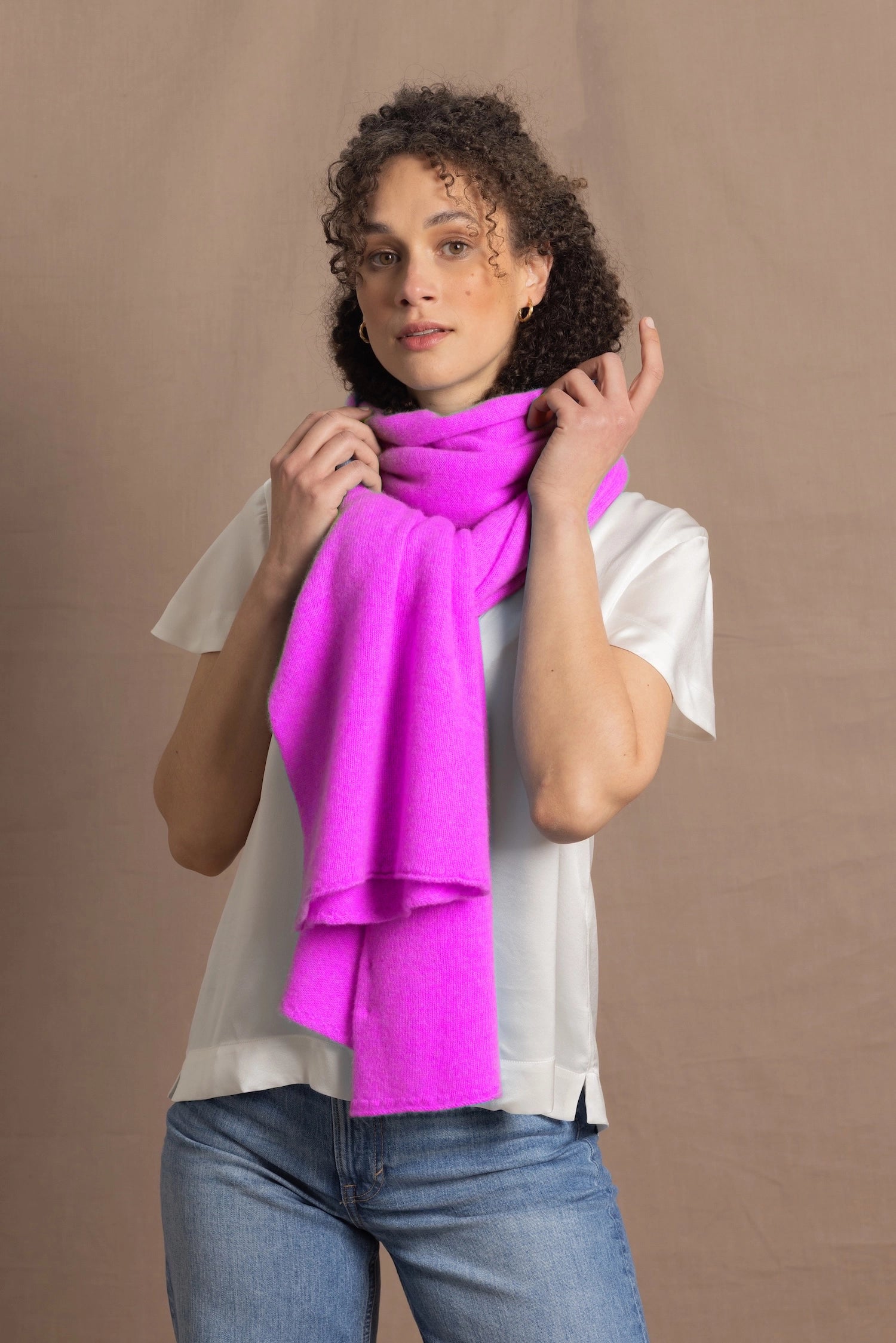 a woman wears a neon pink cashmere scarf wrapped up around her neck over a white silk tee with jeans