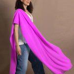 a woman wears a large cashmere wrap shawl in neon pink over a white silk tee with jeans