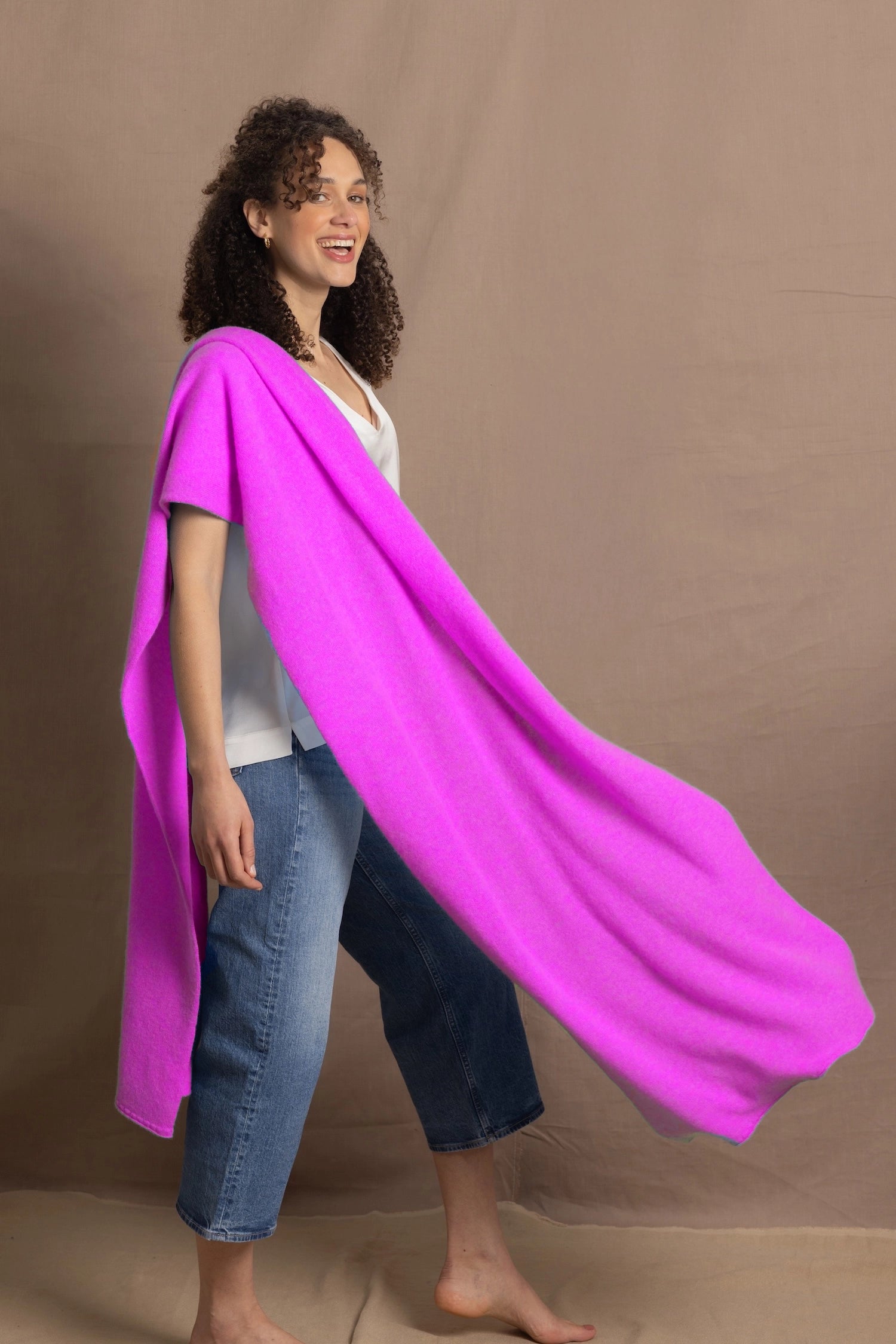 a woman wears a large cashmere wrap shawl in neon pink over a white silk tee with jeans
