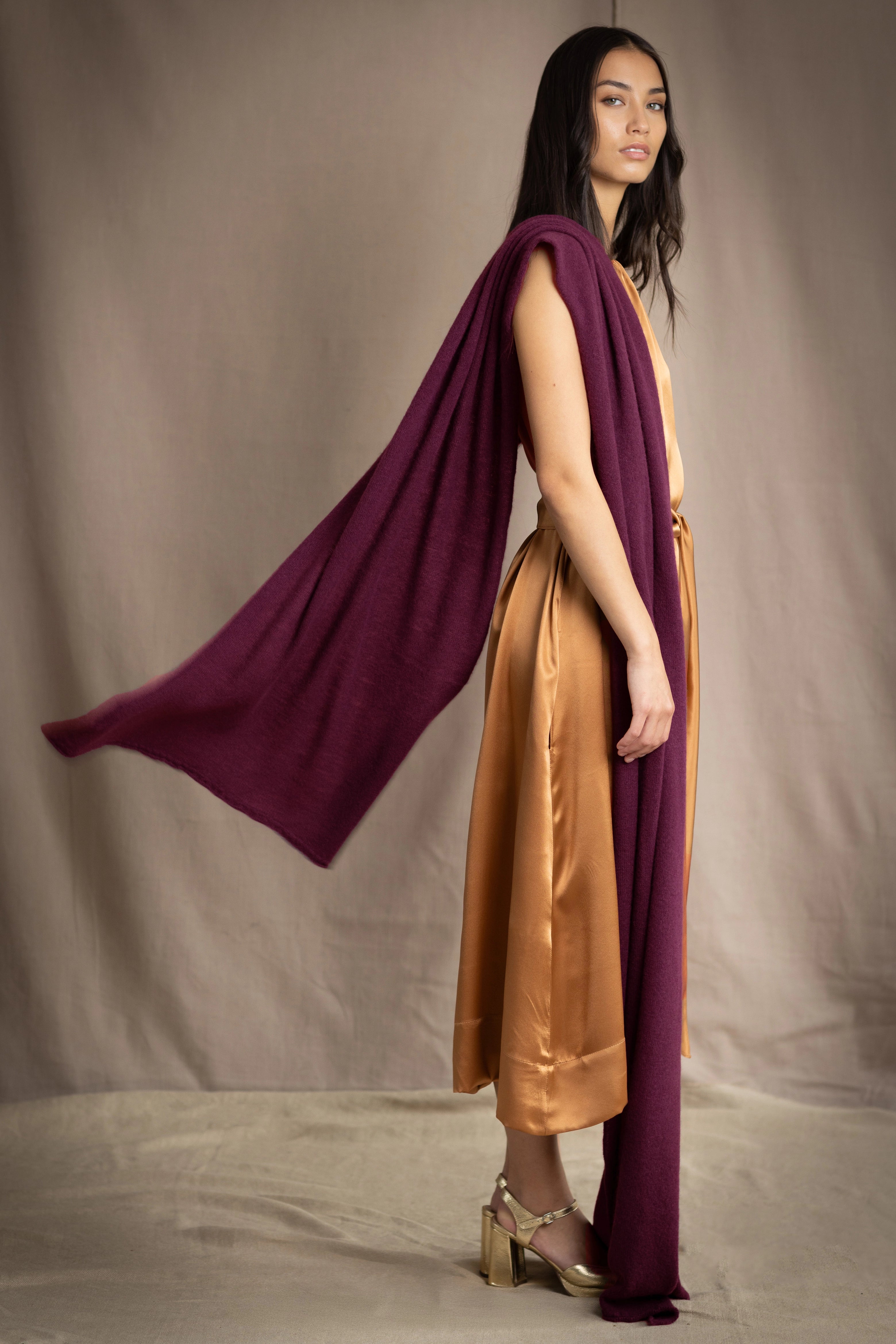 A woman models a deep plum burgundy draped cashmere wrap or shawl over her shoulder