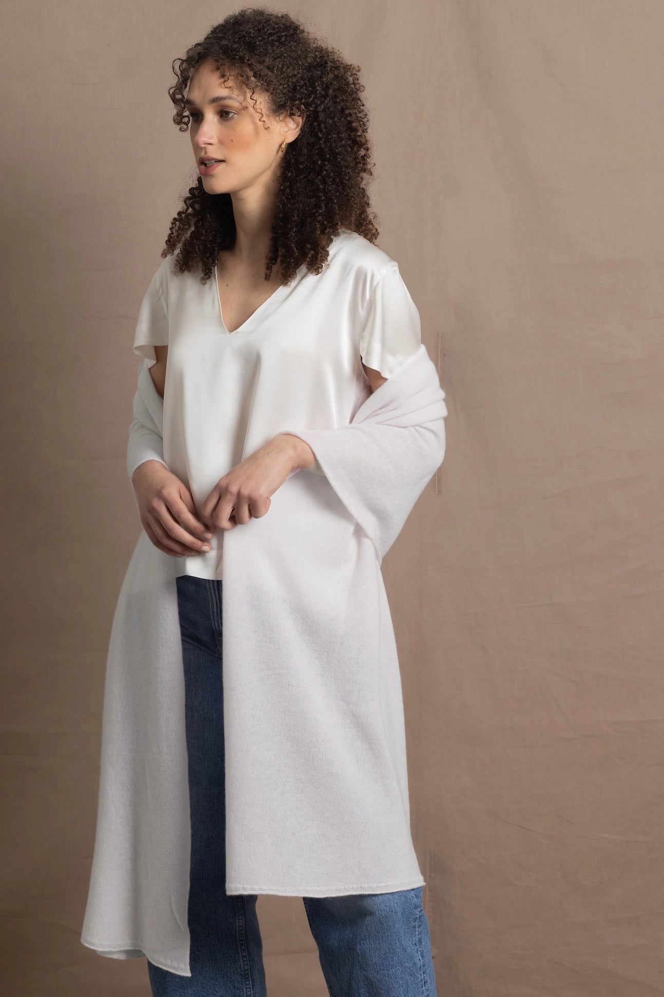 a woman wears a white cashmere wrap shawl over her shoulders with a silk white tee and jeans