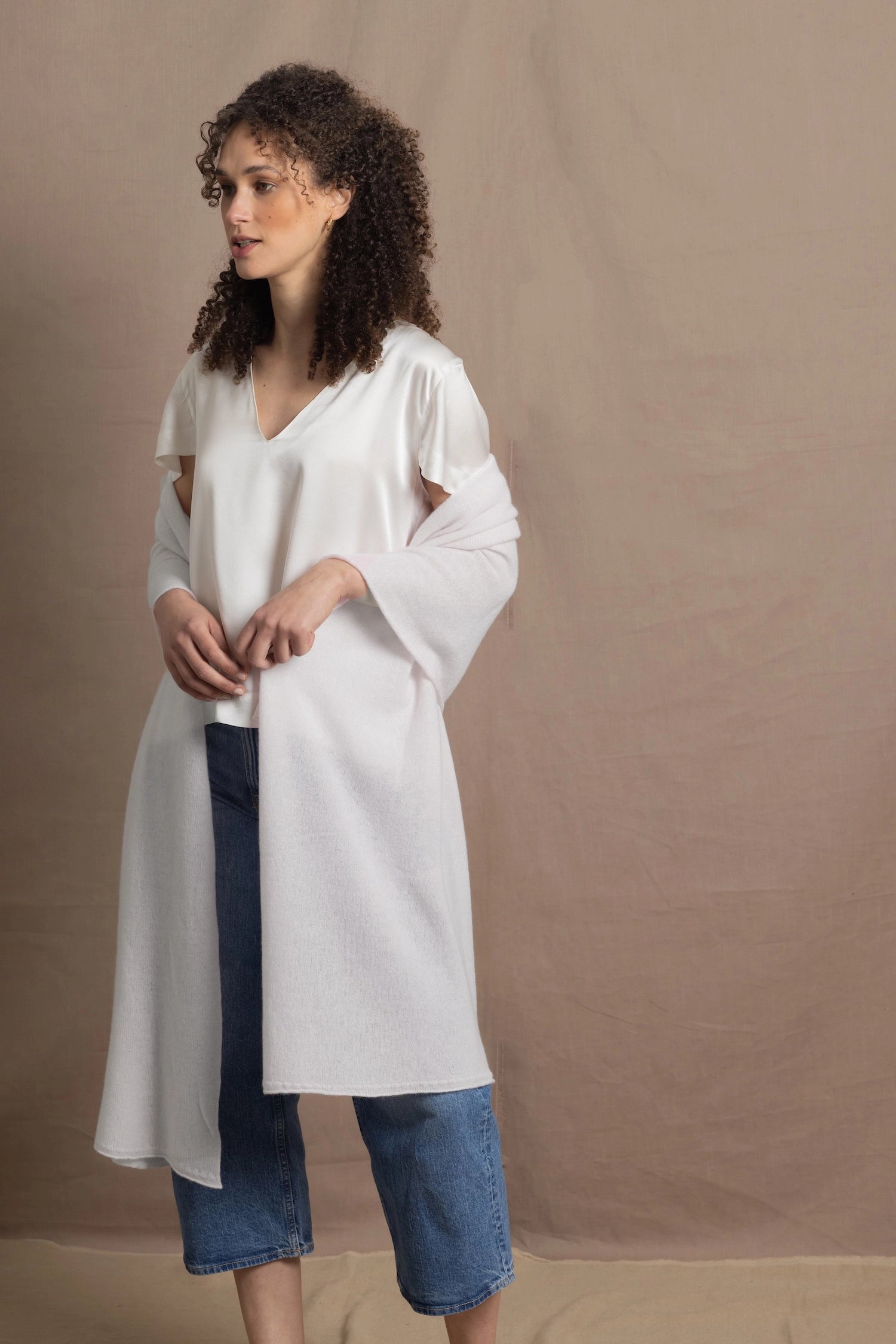a woman wears a white cashmere wrap shawl over her shoulders with a silk white tee and jeans