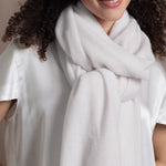 a woman wears a white cashmere wrap scarf tied around her neck with a silk white tee and jeans