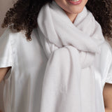 a woman wears a white cashmere wrap scarf tied around her neck with a silk white tee and jeans