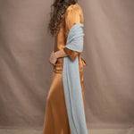 a woman wears a large cashmere wrap shawl in light pale blue turquoise over bronze silk clothing top and skirt