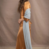 a woman wears a large cashmere wrap shawl in light pale blue turquoise over bronze silk clothing top and skirt