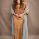 a woman wears a large cashmere wrap shawl in light pale blue turquoise over bronze silk clothing top and skirt