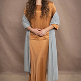 a woman wears a large cashmere wrap shawl in light pale blue turquoise over bronze silk clothing top and skirt