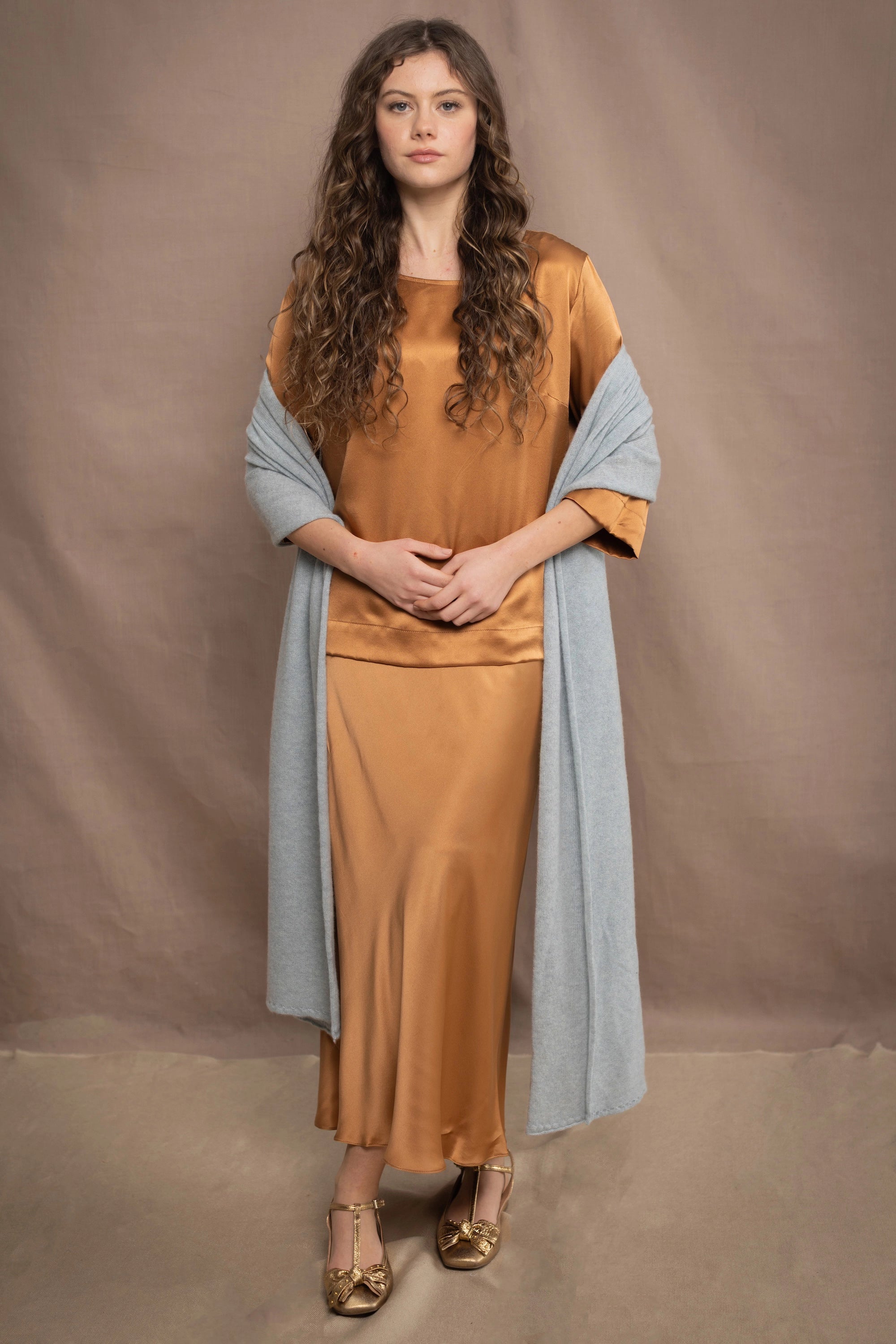 a woman wears a large cashmere wrap shawl in light pale blue turquoise over bronze silk clothing top and skirt